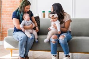 new moms sitting on coach with babies on their laps talking